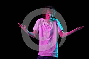 Looks annoyed. Young man with discontent and undercurrent gesturing isolated over dark background in neon light