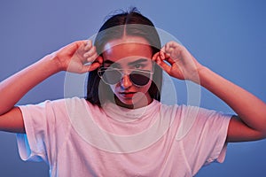 Looks at the camera. Studio shot indoors with neon light. Portrait of beautiful young girl