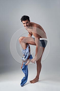 He looks even better with his clothes off. Studio shot of a handsome young man undressing against a grey background.