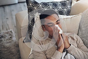 Looks like Im going to go through many tissues today. a young man blowing his nose while feeling sick at home.