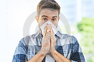 Looks like its flu season again. Portrait of an uncomfortable looking young man blowing his nose with a tissue inside of