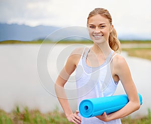 This looks like the perfect spot for some yoga. Portrait of a happy young woman doing yoga next to a lake outside.