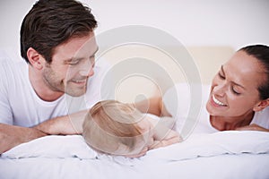 She looks so peaceful when shes asleep...Two loving young parents and their adorable baby girl lying together on a bed.