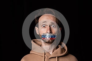 Close-up portrait of young emotive man with three colors duct tape over his mouth isolated on dark background