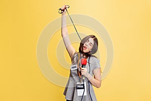 Looks tired. Half-length portrait of young girl, correspondent holding reporter microphone isolated on yellow studio