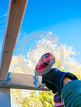Lookup view hand man using cordless impact driver fasten attach exterior wood screws to galvanized joist hanger support underneath
