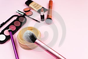 Loose face powder, brush and various cosmetic decorative makeup products on a pink background. Close up. Makeup brush and