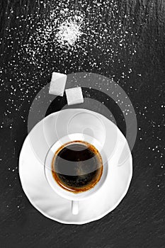 Loose granulated sugar and sugar cubes lie on a slate plate with a cup of coffee