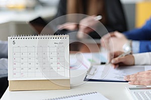 Loose leaf paper calendar standing on table against background of business people closeup