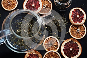 Loose leaf tea next to a glass teapot and dry citrus slices