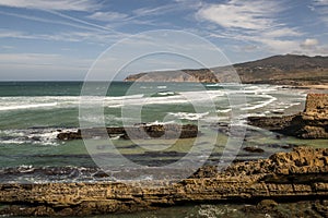 Loose rock cliff and persistent waves on the Portuguese Atlantic coast and a beach with sunbathers on a great summer day