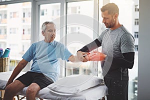 Loosening up all those stiff muscles. a young male physiotherapist assisting a senior patient in recovery.