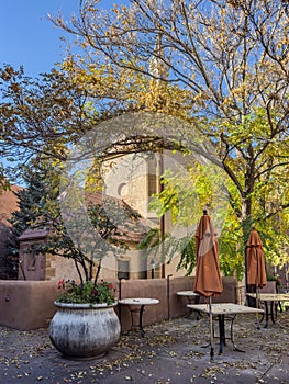 Loretto Chapel in the background of courtyard with trees, folded umbrellas, and tables