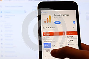 Los Angeles, California, USA - 27 November 2019: Google Analytics app icon on mobile phone screen with blurry website on laptop,