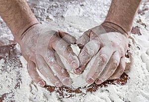 Ð¡lose up of chef human`s hands kneading the dough on the table, powdering with flour. Making dough by hands at bakery or at home