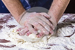 Ð¡lose up of chef human`s hands kneading the dough on the table, powdering with flour. Making dough by hands at bakery or at home