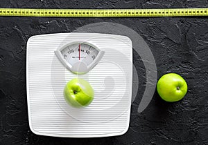 Lose weight concept. Bathroom scale, measuring tape, apples on black background top view