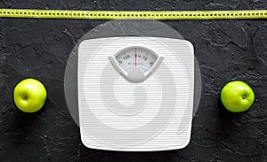 Lose weight concept. Bathroom scale, measuring tape, apples on black background top view