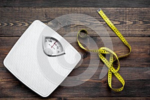 Lose weight concept. Scale and measuring tape on dark wooden background top view