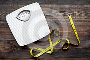 Lose weight concept. Scale and measuring tape on dark wooden background top view