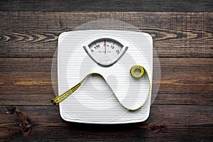 Lose weight concept. Scale and measuring tape on dark wooden background top view