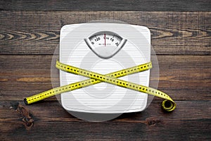 Lose weight concept. Scale and measuring tape on dark wooden background top view