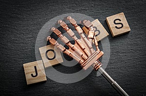 Lose your job to robots due to automation and the rise of the machines concept with a robot hand grabbing wooden tiles that spell
