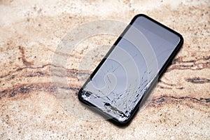 Ð¡loseup black smartphone with broken screen glass lying on wooden table. Concept of dropping phone, broken gadget, electronics