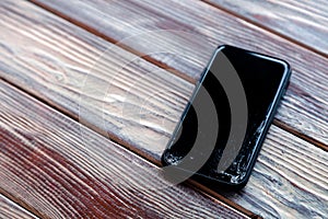 Ð¡loseup black smartphone with broken screen glass lying on wooden table. Concept of dropping phone, broken gadget, electronics