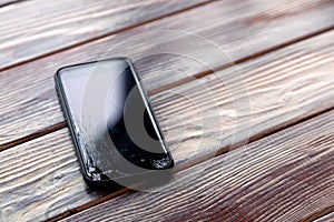 Ð¡loseup black smartphone with broken screen glass lying on wooden table. Concept of dropping phone, broken gadget, electronics