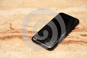 Ð¡loseup black smartphone with broken screen glass lying on wooden table. Concept of dropping phone, broken gadget, electronics