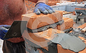 ÃÂ¡loseup of a bricklayer worker installing red bloks and caulking brick masonry joints exterior wall with trowel putty knife