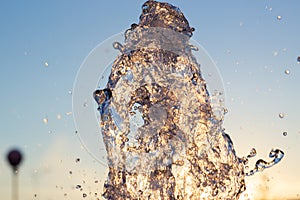 ÃÂ¡loseup jet of water from a fountain hit up against a blue sky, drops of water shimmer in the sun and the rays are reflected.