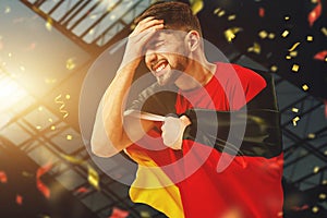 Losing game. Young man, football fan with german flag cheering up football team over dark background with confetti