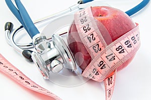 Losing weight with healthy food fruits and vegetables under doctor supervision. Red apple wrapped up by measuring tape and steth