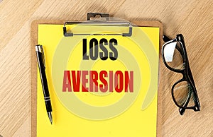 LOSS AVERSION text on yellow paper on clipboard with pen and glasses photo