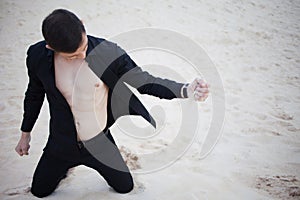 Loss, concept. young man kneeling in the desert. Sand through fingers