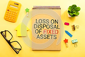 Loss on disposal of fixed assets label on notepad with laptop and smartphone on wooden table.
