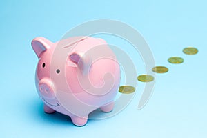 Loss of money. Pink piggy bank losing gold coins on blue background. Bad investment or falling profits