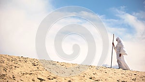 Lost Bedouin with staff walking in hot desert, climate change, hopelessness