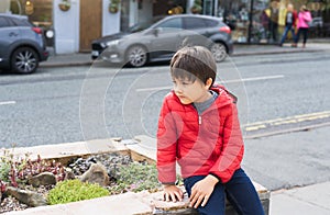 Lost Kid sitting alone next to a busy street in a center of city, Young boy with worrying face looking looking out deep in