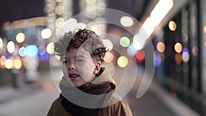 lost little child is walking on street in night, curly boy is going alone in city district