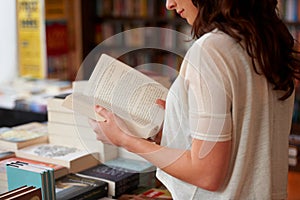 Lost in the pages. A cropped shot of a young woman reading a book while standing in a bookstore.