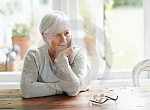 Lost in pleasant memories. A senior woman sitting at her kitchen table lost in thought.