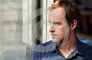 Lost in thought. Shot of a man looking thoughtfully through a window.