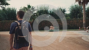 Lost tourist man is walking in tropical garden area of park , back view