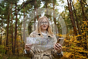 Lost traveler young woman with phone searching direction in with a Topographic Map in the forest. High quality photo