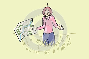 Lost woman with map stands in field and shrugs shoulders, not knowing where to go to find way home