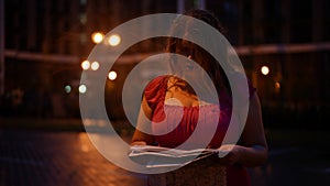 Lost woman with paper map standing on empty city street at night looking around. Portrait of unsure Caucasian plus-size