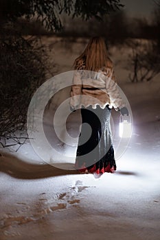 Lost young woman in the winter forest with a lantern